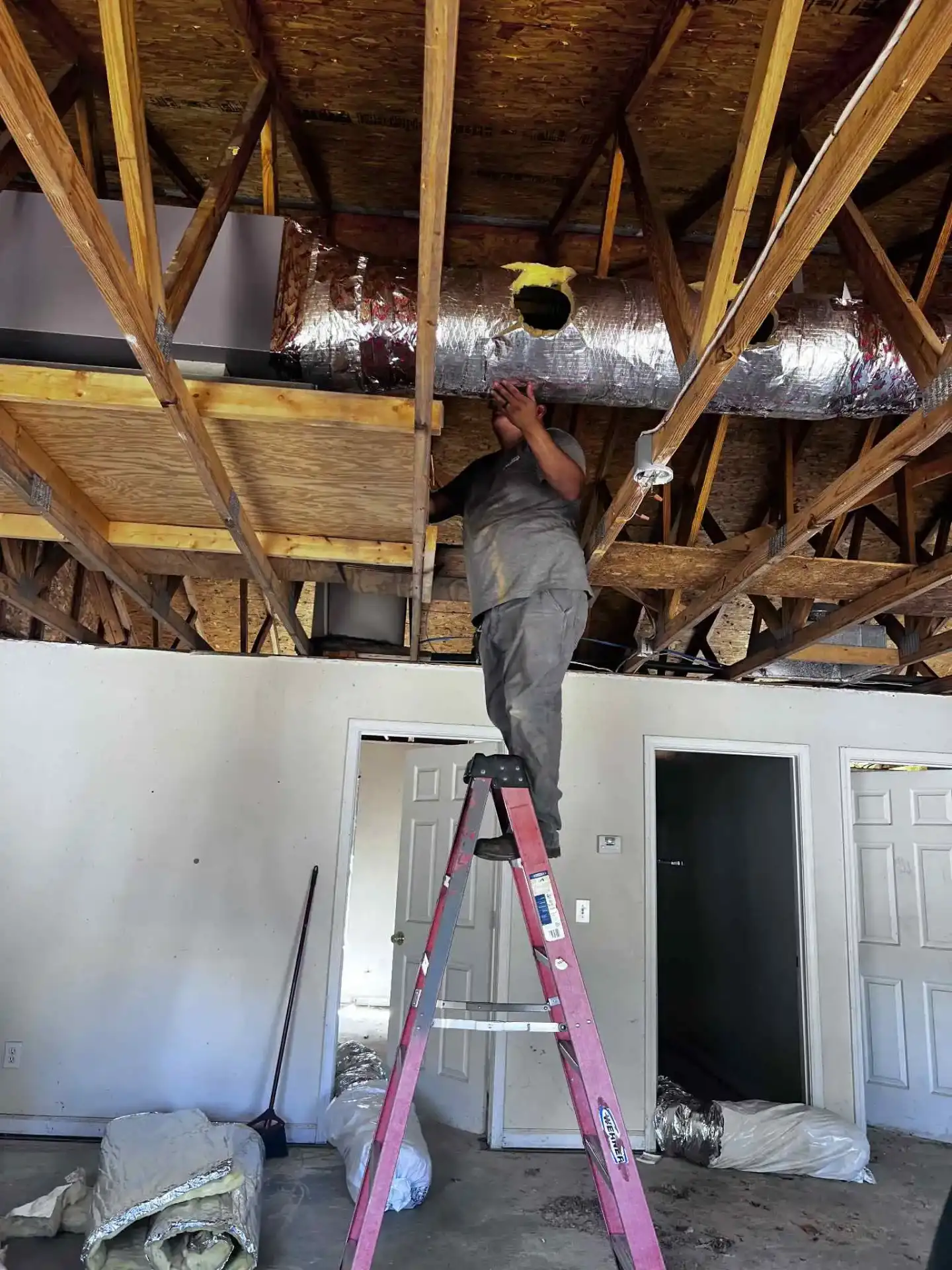 Dependable HVAC technician on ladder working on ceiling ductwork